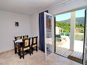 A balcony with a table and chairs, a view of a hillside, and a door leading to an outdoor area.