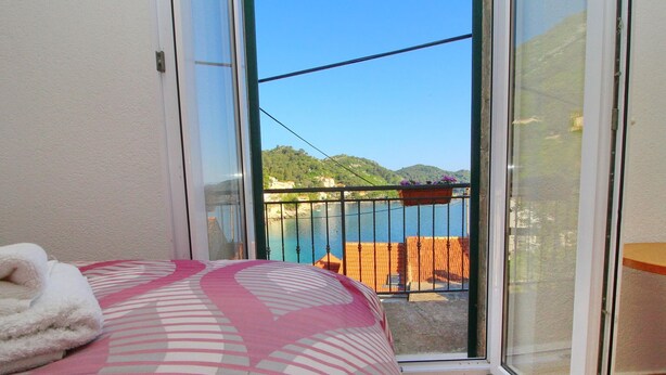 A bedroom with a bed, a window, and a view of a balcony with a railing and a body of water. - Apartment Mambo , Mljet - Duplex Apartment With Terrace and Sea View (Mljet)