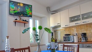 A modern kitchen with a blue tablecloth, a TV mounted on the wall, and a window with curtains. - Apartment Mambo , Mljet - Duplex Apartment With Terrace and Sea View (Mljet)