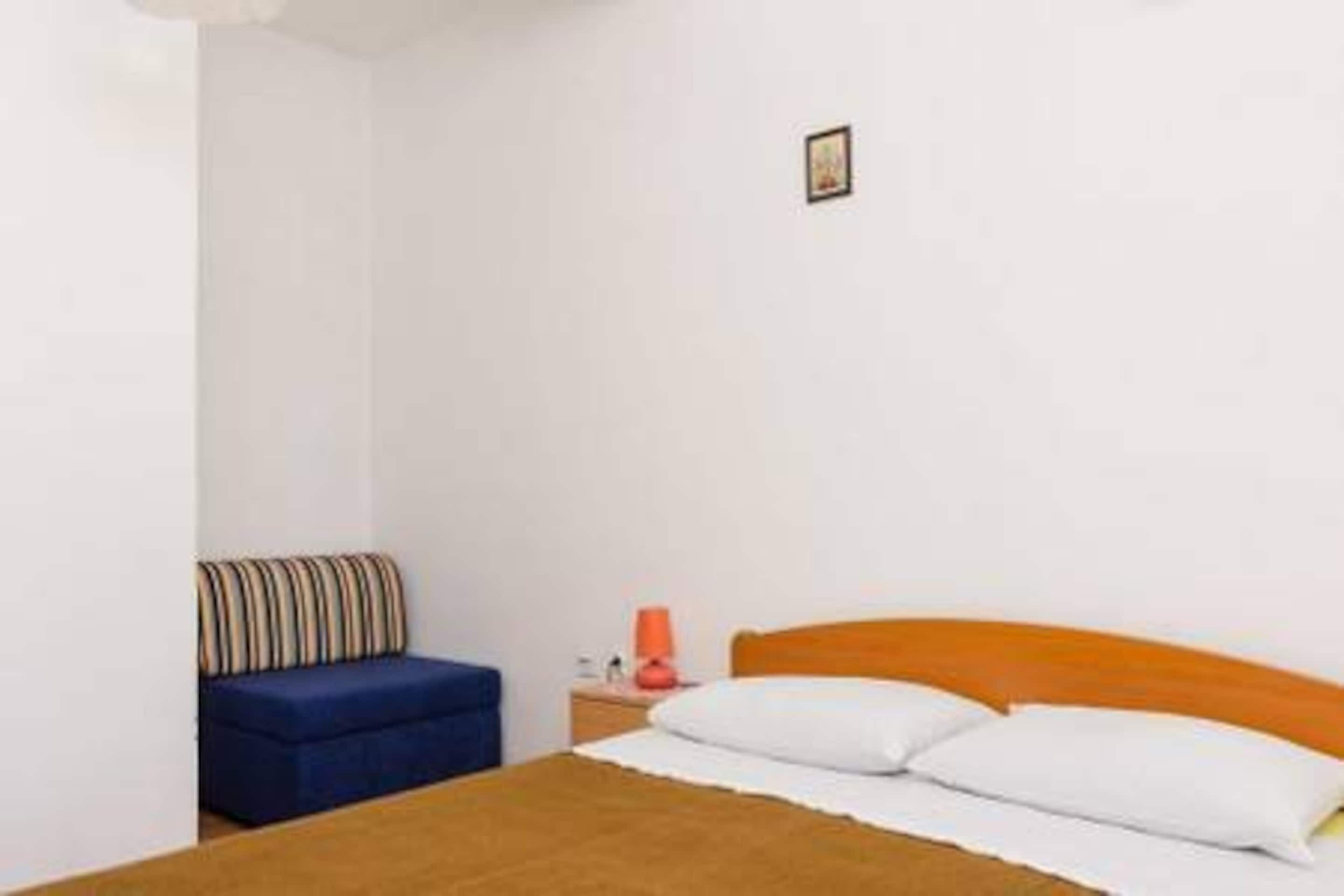 A bedroom with a single bed, a blue sofa, a nightstand with a lamp, and a small framed picture on the wall.