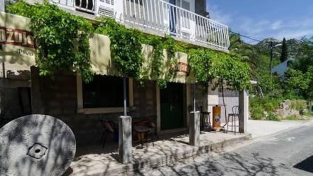 A building with a balcony, a signboard, and a large circular object on the ground. - Apartments Felix Mljet - One Bedroom Apartment With Balcony (Mljet)