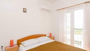 A bedroom with a bed, a nightstand, a window with curtains, and an air conditioning unit. - Apartments Felix Mljet - One Bedroom Apartment With Balcony (Mljet)
