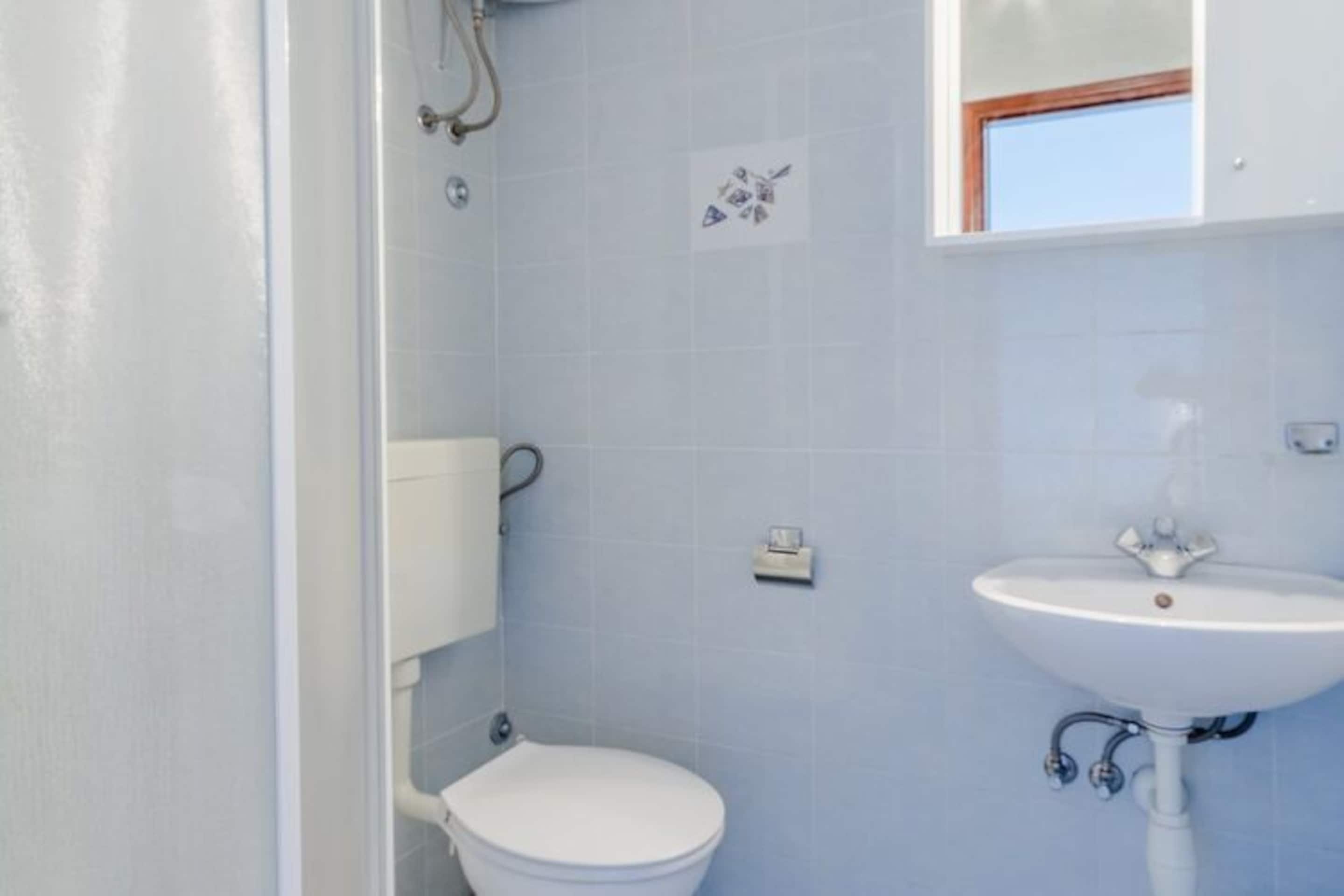 Et badeværelse med toilet, håndvask og et vindue over vasken.