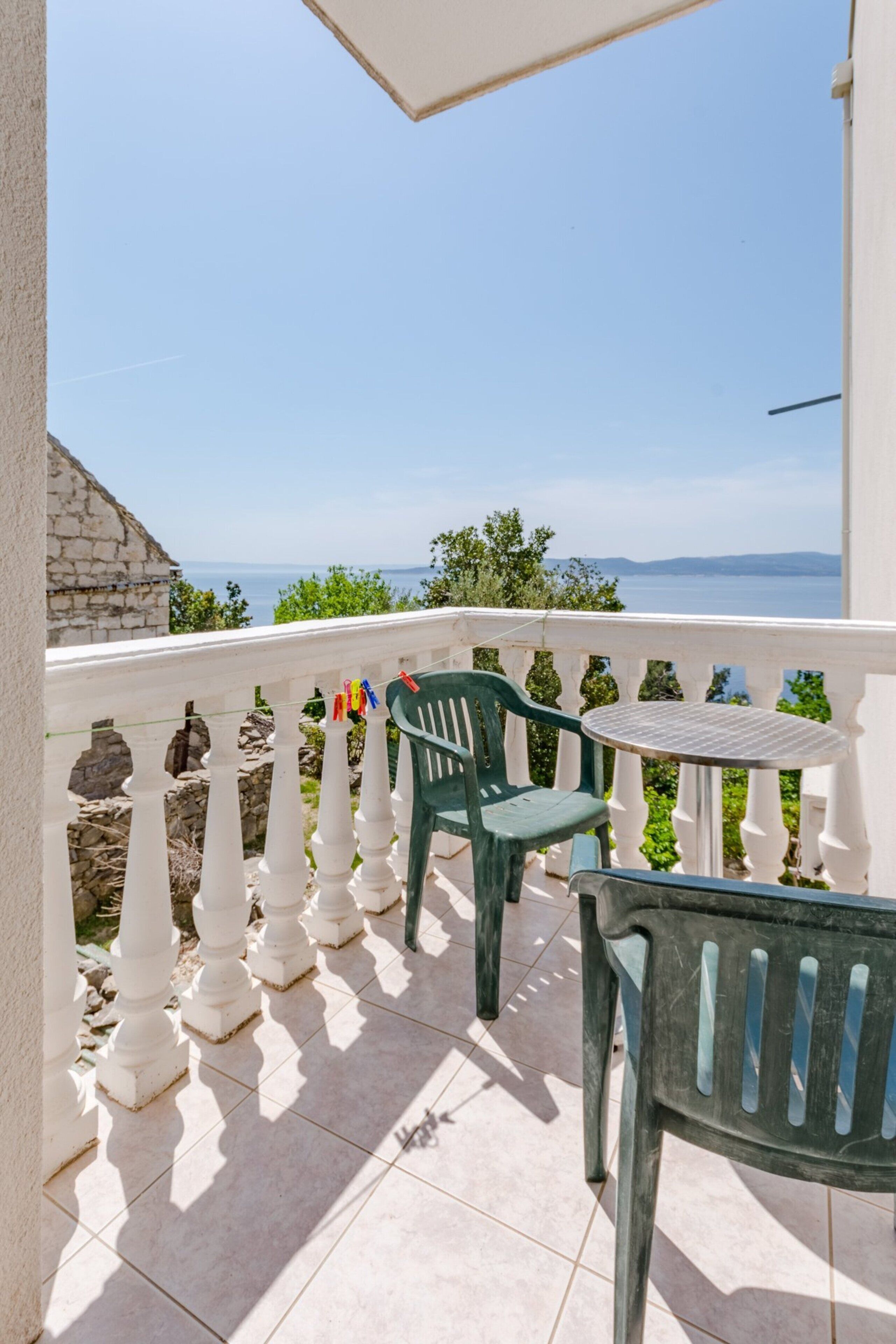 A balcony with white balustrades, a green plastic chair, and a small round table.