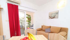 Et spiseområde med et træbord, et fad med frugt, en rød gardin, en beige sofa og et billede på væggen.
