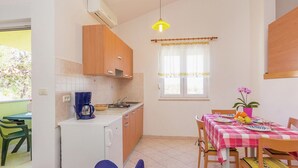 A compact kitchen with a coffee maker, a sink, and wooden cabinets. There is a dining table with a checkered tablecloth and chairs. - Apartment in Premantura With Seaview Balcony (Medulin)