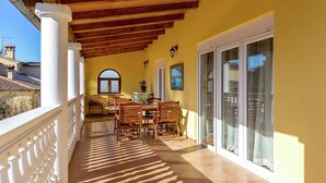 Un patio cubierto con una mesa y sillas de madera, una planta en maceta y vistas del entorno.