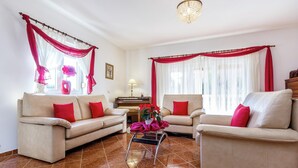 Una sala de estar con dos sofás color beige, cojines rojos, una mesita con una planta y una araña.