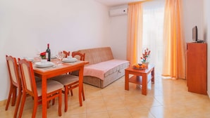 Un espacio habitable compacto con comedor, sofá, una mesita con fruta y televisor sobre un mueble.