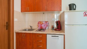 Una cocina compacta con armarios de madera, un lavamanos, una cafetera y un lavavajillas.