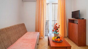 Una sala de estar con un sofá, una mesa con fruta, un televisor sobre un mueble de madera y una ventana con cortinas.