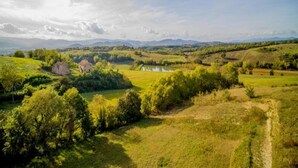 Un paysage rural caractérisé par des collines douces, un petit plan d’eau et quelques bâtiments dispersés.
