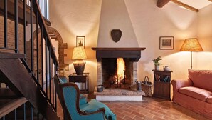 Un salon chaleureux avec une cheminée, des poutres en bois, un escalier et des sièges confortables.