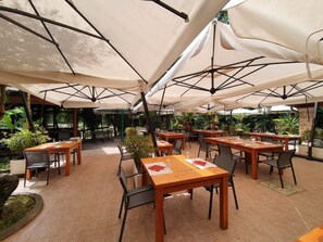 An outdoor dining area with multiple wooden tables and chairs, covered by large white umbrellas. - Belvilla by OYO Veio 4 pax (Rome)