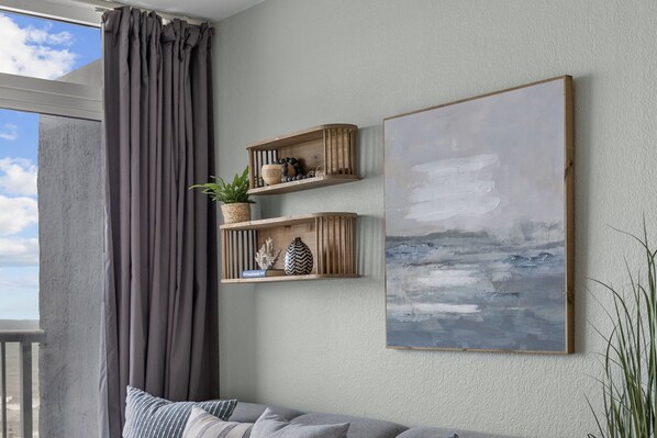 Una habitación con una cortina gris, un sofá gris y dos estantes de madera con adornos.