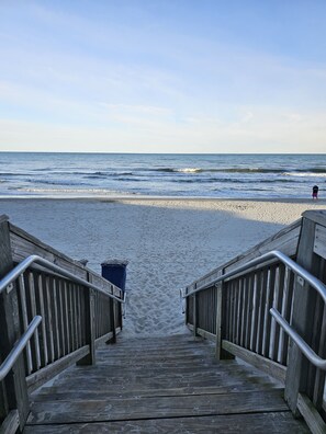A wooden staircase leading to a sandy beach with a view of the ocean.