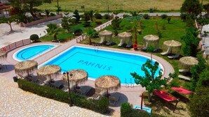 Une piscine dont la surface de l’eau porte l’inscription « PAHNS », entourée de chaises longues et d’ombrelles en feuilles de palmier.