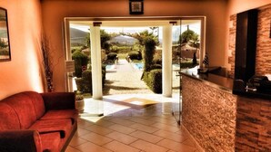 Un espace d’accueil avec un canapé rouge, un comptoir de réception et une vue sur une piscine et un jardin.