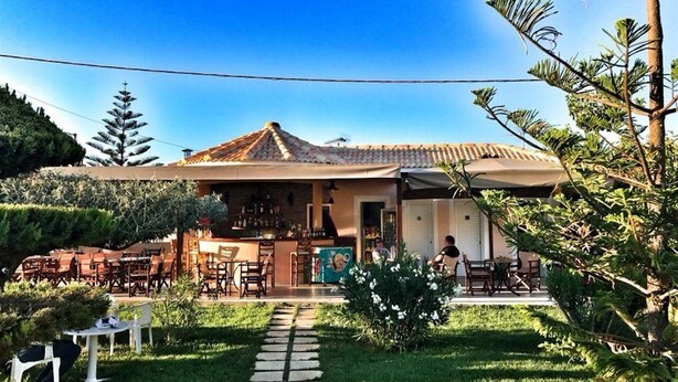 Un restaurant doté d’une terrasse, d’un toit recouvert de tuiles et d’un chemin qui traverse le jardin.