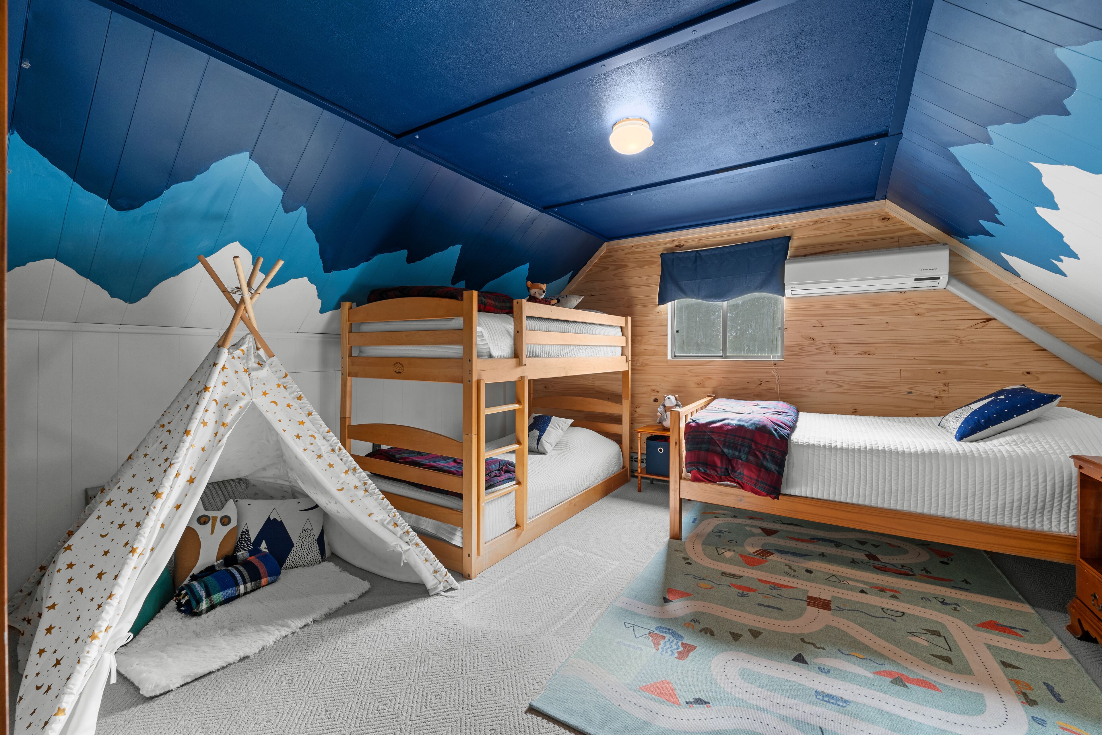Un dormitorio abrigado en el ático con una cama nido, una pequeña tienda de campaña y una ventana.