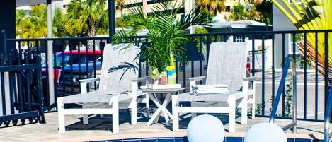 A poolside area with white lounge chairs, a small table with drinks, and two white floating balls.