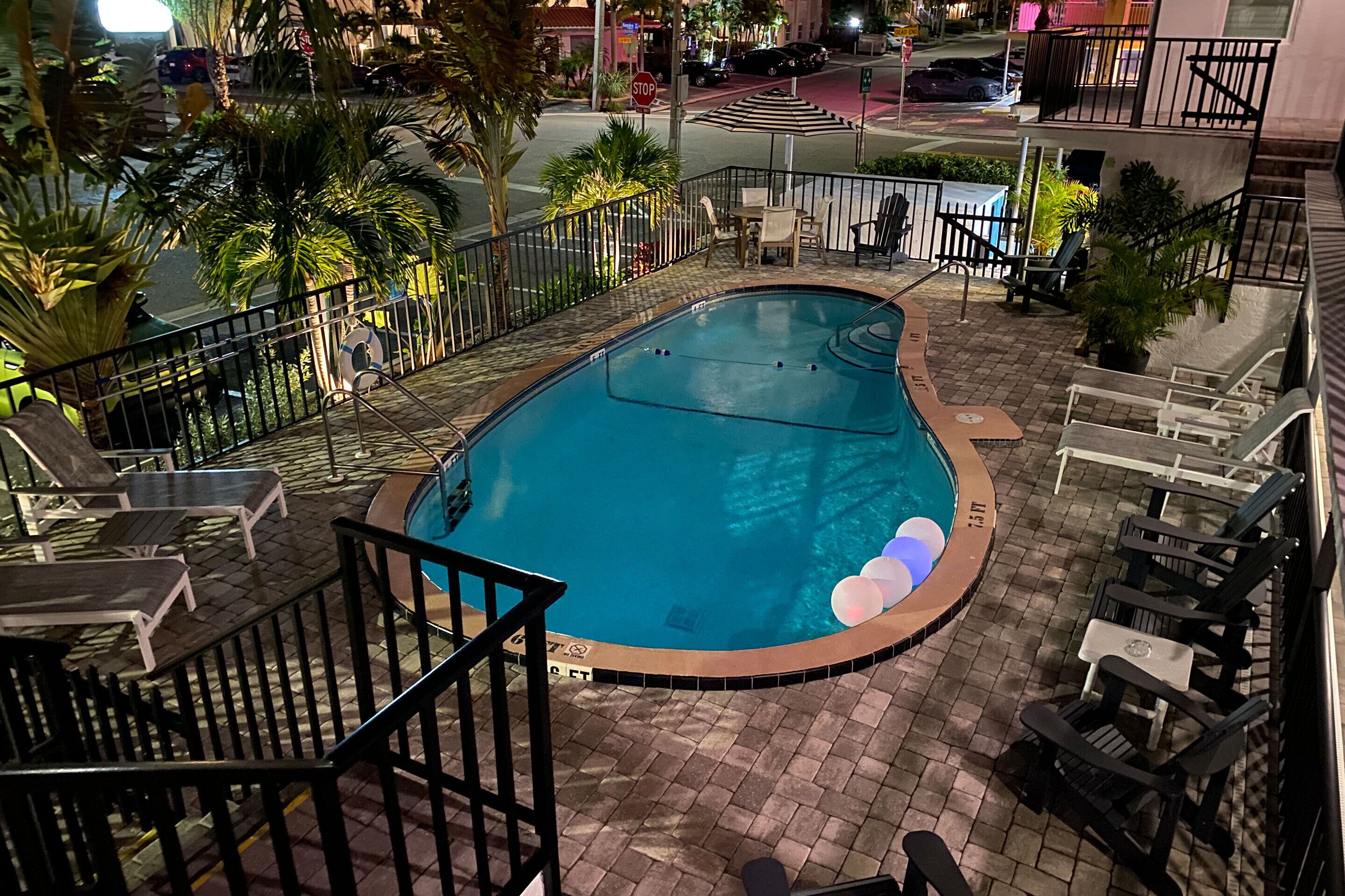 Una piscina en la azotea con solárium de baldosas, rodeada de palmeras y mobiliario para exteriores.