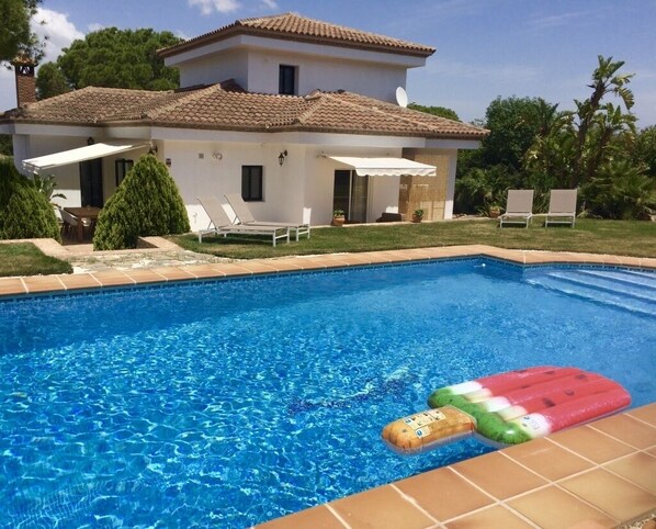 A swimming pool with a floating mat, a white house with a tiled roof, and a well-maintained lawn. - Villa Pinos Malaga (Alhaurin de la Torre)