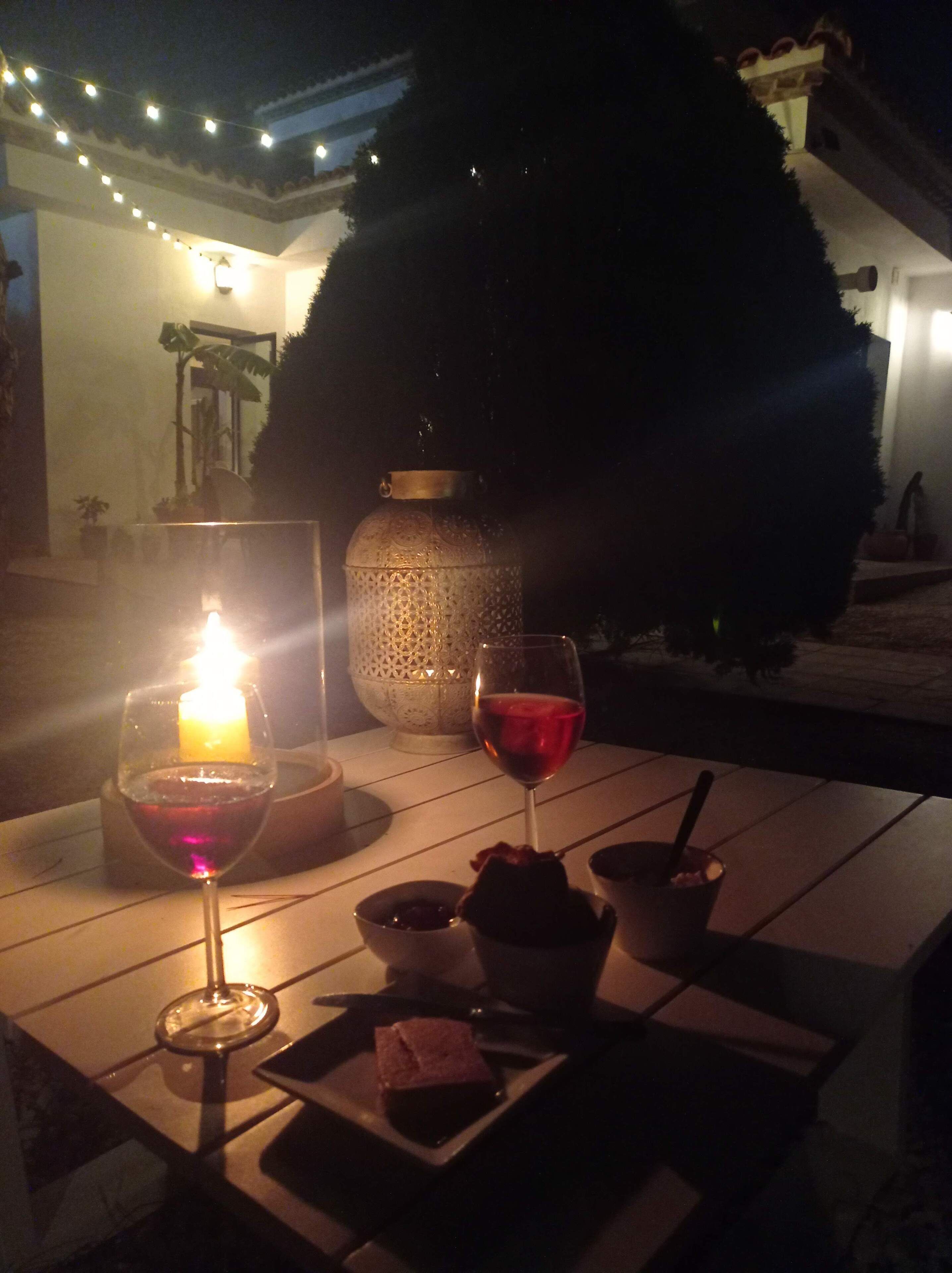 Un área de comedor al aire libre con una mesa iluminada por velas, copas de vino y un postre.
