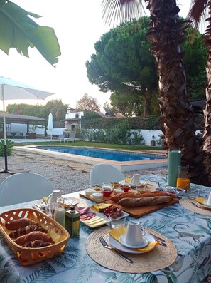 An outdoor dining area with a pool view, featuring a table set with breakfast items, a large umbrella, and a tropical-themed tablecloth. - Villa Pinos Malaga (Alhaurin de la Torre)