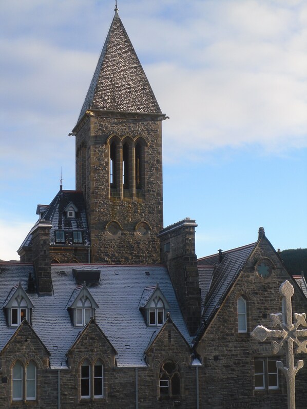 A historic stone building with a prominent tower featuring arched windows and a pointed roof. - Stunning apartment in a historic setting with a shared pool on the shores of Loch Ness (Fort Augustus)