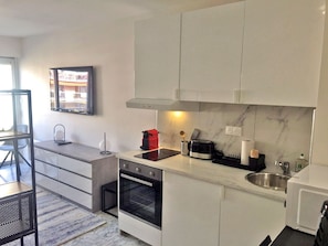 A modern kitchen with white cabinets, a built-in oven, a microwave, and a sink.