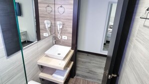 Une salle de bain moderne équipée de toilettes, d’un lavabo et d’un espace douche. Deux porte-serviettes sont fixés au mur et un miroir se trouve au-dessus du lavabo.