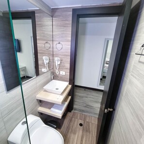 A modern bathroom with a toilet, a sink, and a shower area. There are two towel rings on the wall and a mirror above the sink.