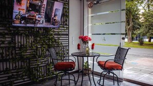 Een buitenruimte met twee metalen stoelen en een kleine tafel, omringd door een decoratieve muur begroeid met klimplanten.