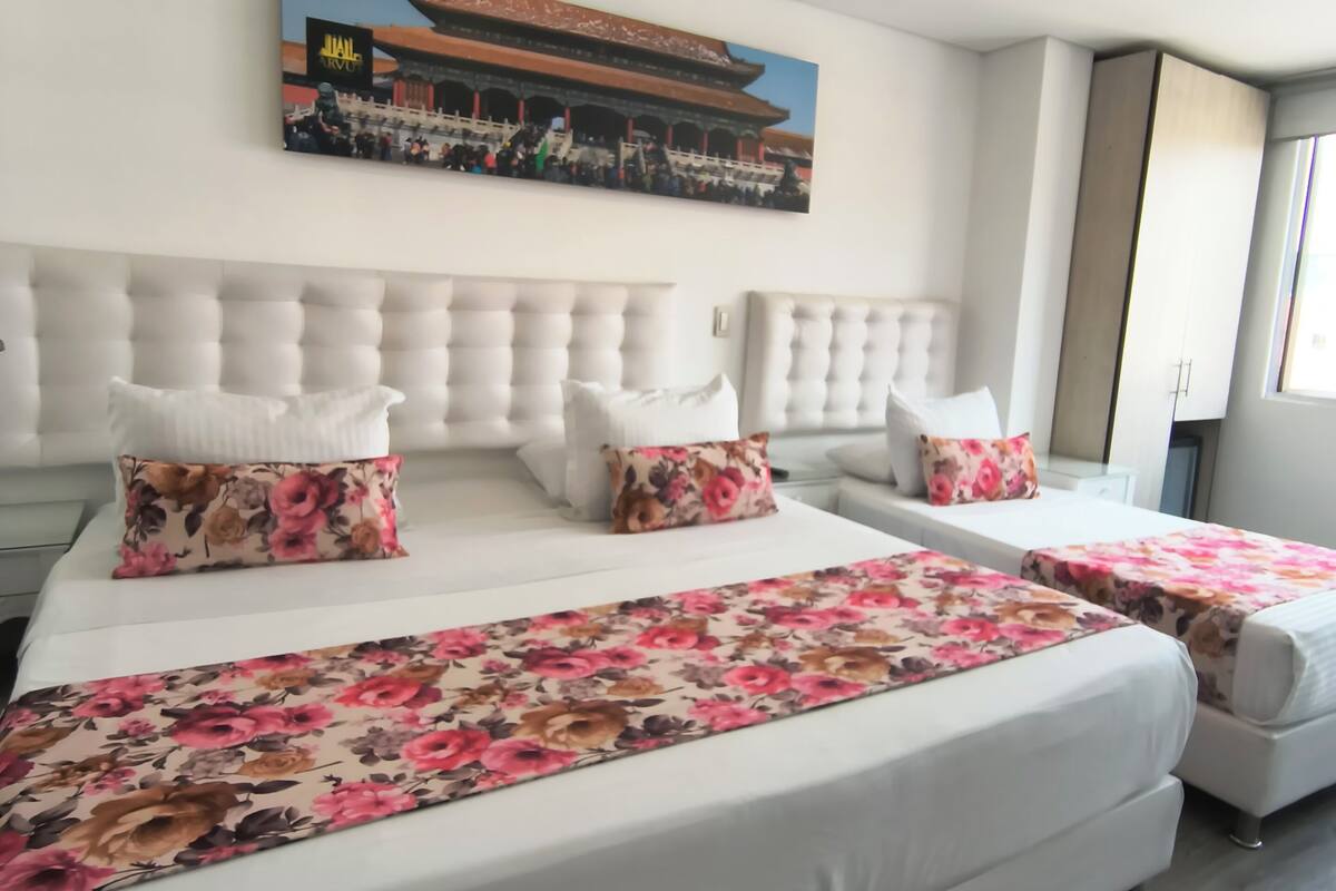A hotel room with a large bed, a headboard, a painting of a building, and a window.