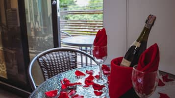 Una mesa con una botella de champán y dos copas, ambas con servilletas rojas, rodeada de pétalos de rosa.