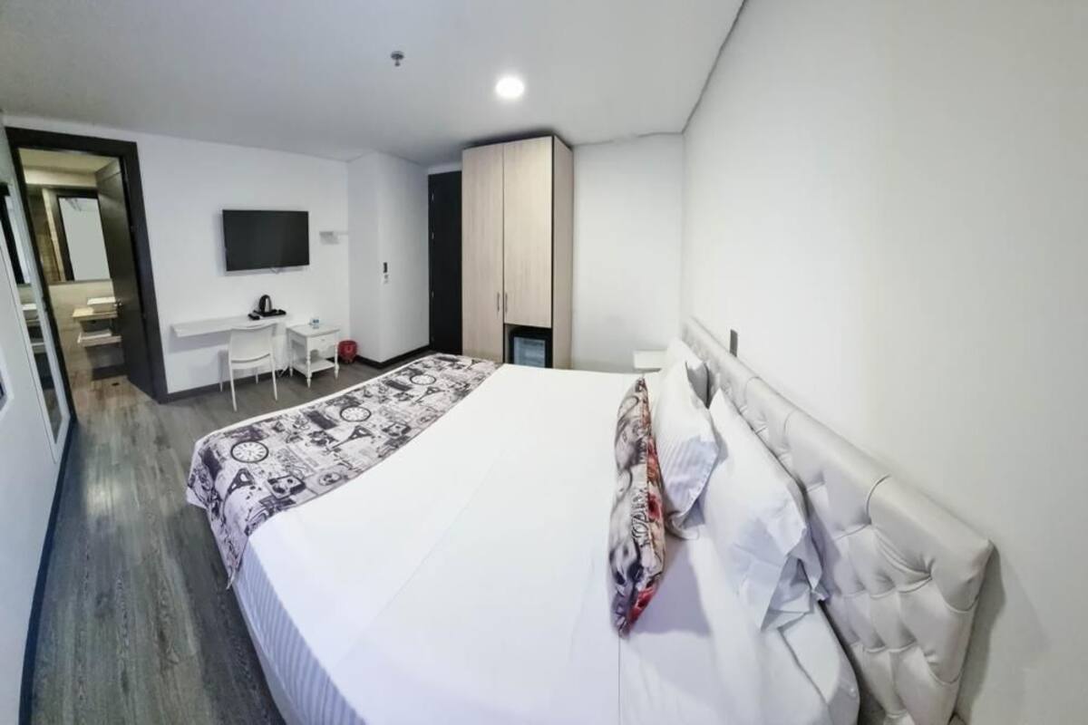 A hotel room with a large bed, a desk with a chair, a television, and a wardrobe.