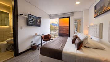 Habitación de hotel moderna con cama, escritorio, silla, televisor mostrando un mensaje de bienvenida y balcón con vistas al desierto.