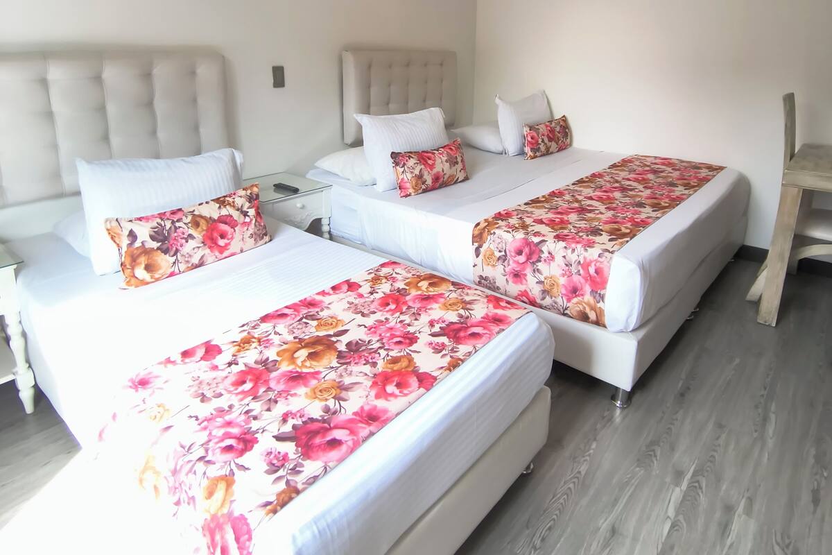 A hotel room with three beds, each with floral bedding, a wooden floor, and a white ceiling.