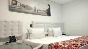 Een hotelkamer met een groot bed, een ronde glazen tafel, een wit hoofdeinde en een schilderij van een stadsgezicht aan de muur.