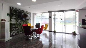Un espace intérieur moderne avec une porte vitrée donnant sur l’extérieur, un mur en métal noir agrémenté de plantes et un coin salon avec des chaises rouges et jaunes.