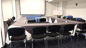 Een vergaderruimte met een lange tafel, stoelen, een projectiescherm en een whiteboard.