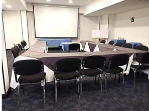Une salle de conférence équipée d’une longue table, de chaises, d’un écran de projection et d’un tableau blanc.