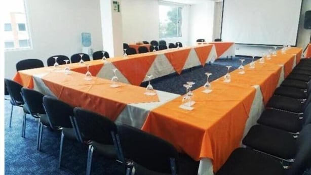 Une salle de conférence avec une longue table, des chaises noires et des nappes orange.