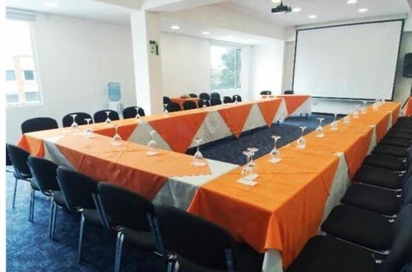 Konferenssihuone, jossa on pitkä pöytä, mustat tuolit ja oranssit pöytäliinat.