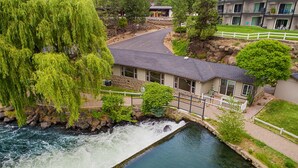 Un hotel a orillas del río con fachada de piedra, una pequeña cascada y una valla blanca.