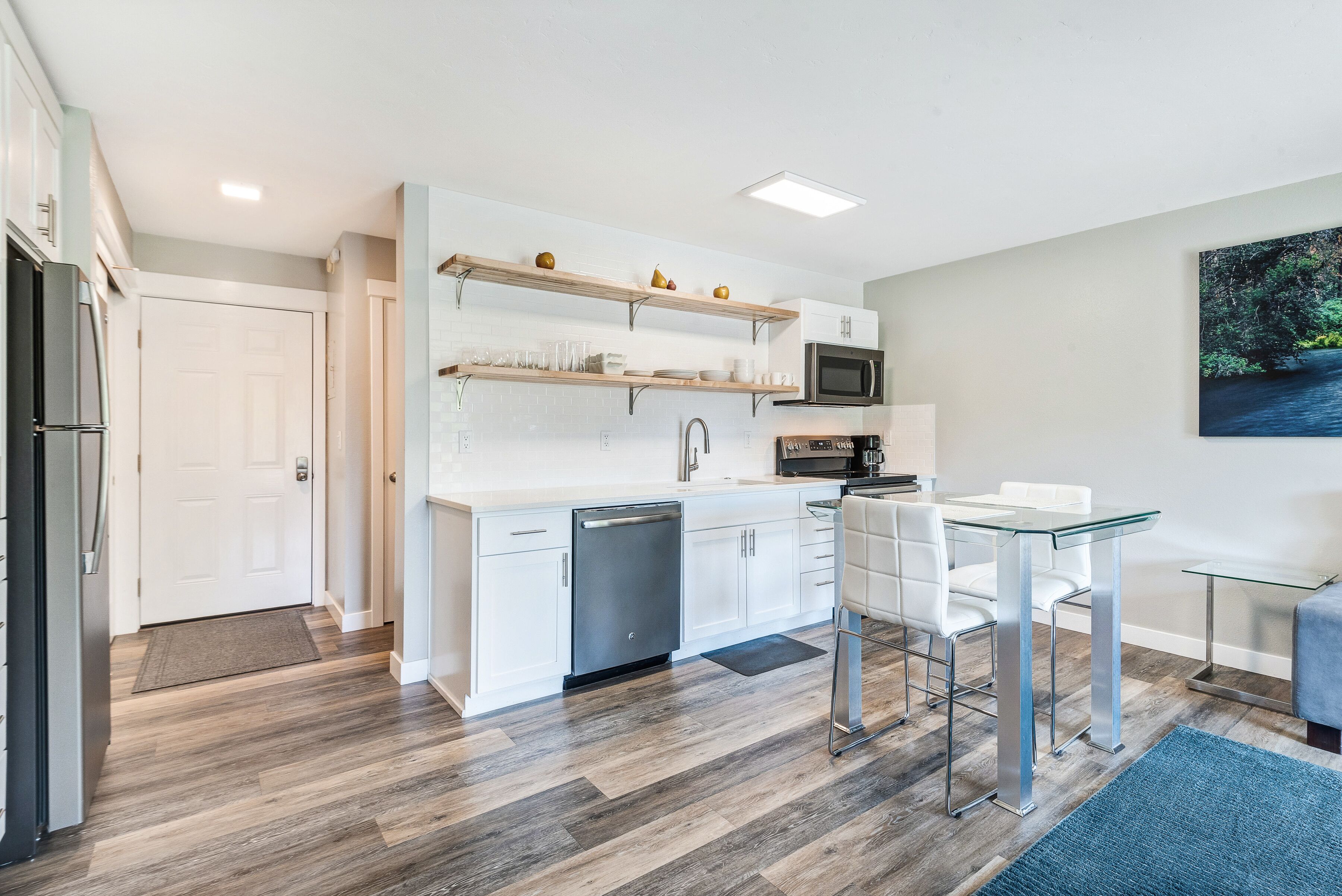 A modern kitchen with white cabinets, a dishwasher, a microwave, and a dining area with a glass table and chairs.