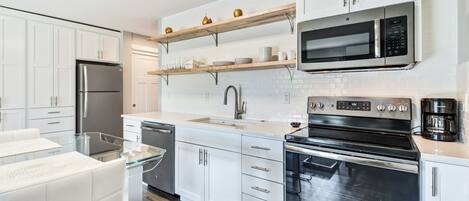 Une cuisine moderne avec des meubles blancs, des appareils en acier inoxydable et des étagères en bois.
