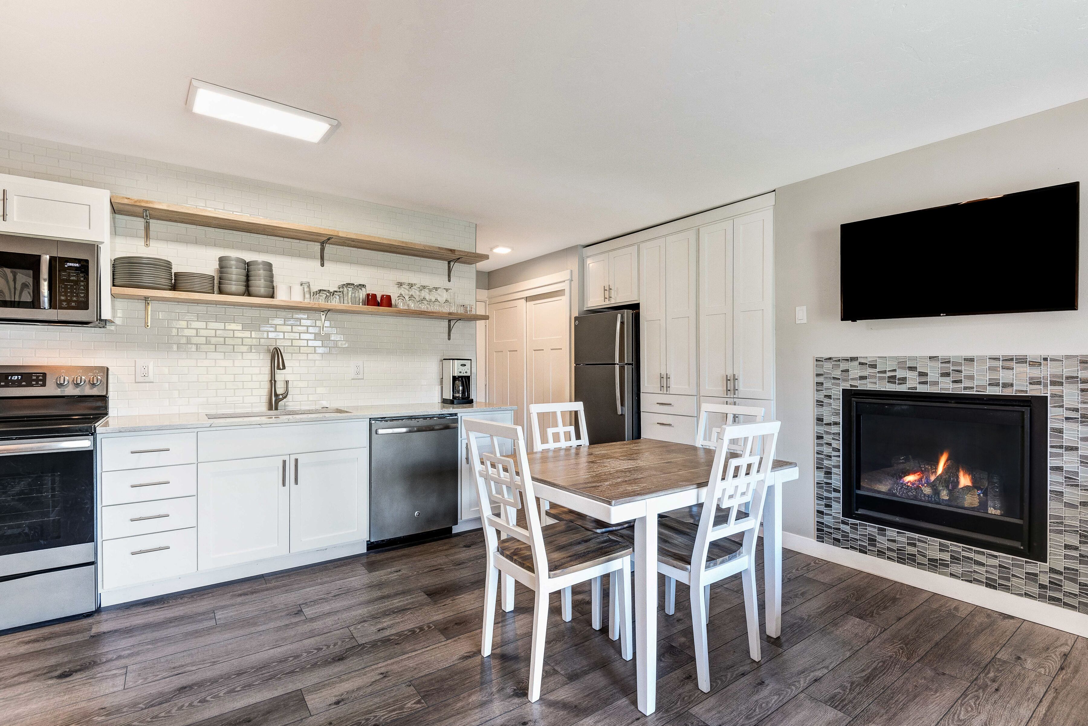 A modern kitchen with white cabinetry, a built-in microwave, a stainless steel refrigerator, and a dining area with a wooden table and white chairs.