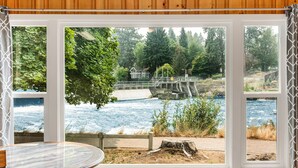 Una habitación con un amplio ventanal con vistas a un río, un banco de madera y una mesa.